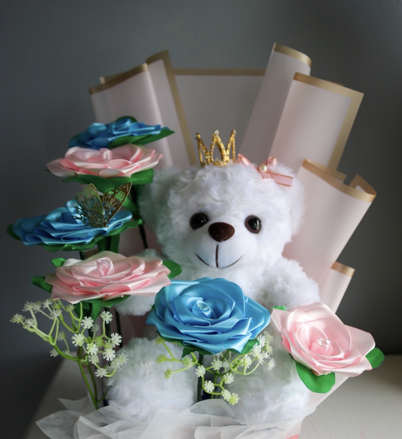 Arreglo de rosas de listón rosas y azules con osito de peluche y corona